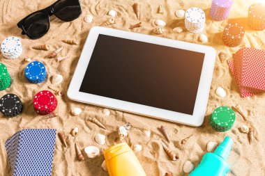 Online poker oyunu ile dijital tablet ve fiş destesi şeklinde sahilde. Üstten Görünüm. Uzay kopyalayın. Düz yatıyordu. Güneş parlaması
