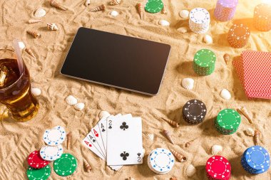 Online poker oyunu ile dijital tablet ve fiş destesi şeklinde sahilde. Üstten Görünüm. Uzay kopyalayın. Düz yatıyordu. Güneş parlaması