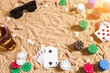 Plaj pokeri. Çipler ve kartlar kumsalda. Deniz kabuklarının, güneş gözlüklerinin ve soğuk bir bardağın etrafında. Üst Manzara. Uzayı kopyala Düz yatıyordu. Güneş parlaması