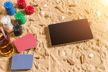 Online poker oyunu ile dijital tablet ve fiş destesi şeklinde sahilde. Üstten Görünüm. Uzay kopyalayın. Düz yatıyordu. Güneş parlaması