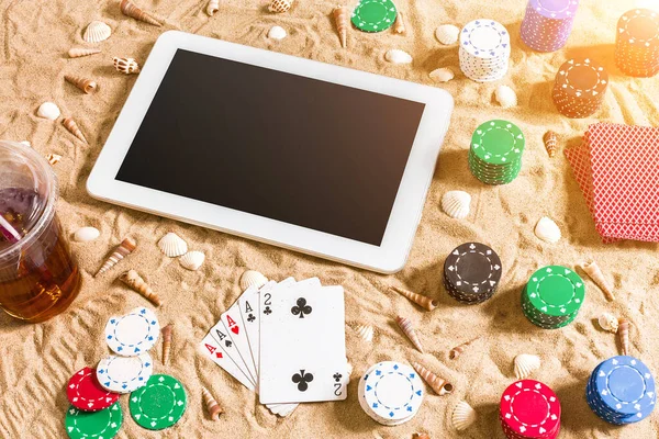 Online poker game on the beach with digital tablet and stacks of chips. Top view. Copy space. Flat lay. Sun flare
