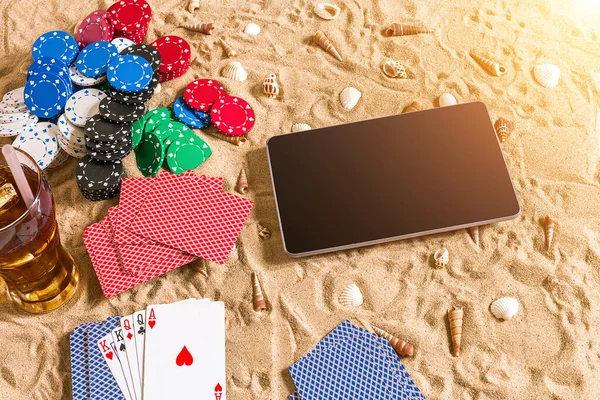 Online poker game on the beach with digital tablet and stacks of chips. Top view. Copy space. Flat lay. Sun flare