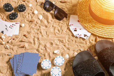 Plaj pokeri. Çipler ve kartlar kumsalda. Deniz kabuklarının, güneş gözlüklerinin ve parmak arası terliklerin etrafında. Üst Manzara. Uzayı kopyala Düz yatıyordu. Güneş parlaması