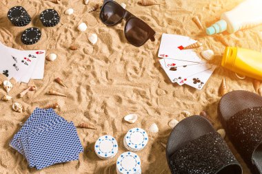 Plaj pokeri. Çipler ve kartlar kumsalda. Deniz kabuklarının, güneş gözlüklerinin ve parmak arası terliklerin etrafında. Üst Manzara. Uzayı kopyala Düz yatıyordu. Güneş parlaması