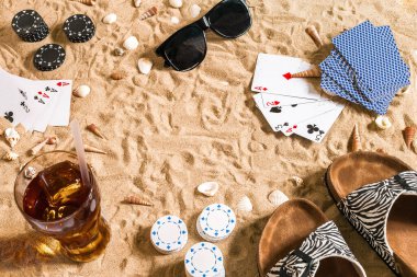 Plaj pokeri. Çipler ve kartlar kumsalda. Deniz kabuklarının, güneş gözlüklerinin ve parmak arası terliklerin etrafında. Üst Manzara. Uzayı kopyala Düz yatıyordu