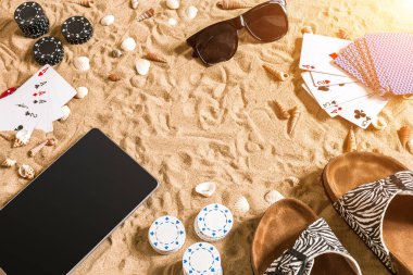 Online poker oyunu ile dijital tablet ve fiş destesi şeklinde sahilde. Üstten Görünüm. Uzay kopyalayın. Düz yatıyordu. Güneş parlaması