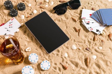 Online poker oyunu ile dijital tablet ve fiş destesi şeklinde sahilde. Üstten Görünüm. Uzay kopyalayın. Düz yatıyordu