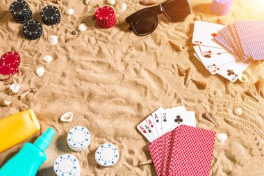 Plaj pokeri. Çipler ve kartlar kumsalda. Deniz kabukları, güneş gözlüğü ve güneş kremi. Üst Manzara. Uzayı kopyala Düz yatıyordu. Güneş parlaması