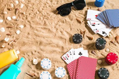 Plaj pokeri. Çipler ve kartlar kumsalda. Deniz kabukları, güneş gözlüğü ve güneş kremi. Üst Manzara. Uzayı kopyala Düz yatıyordu