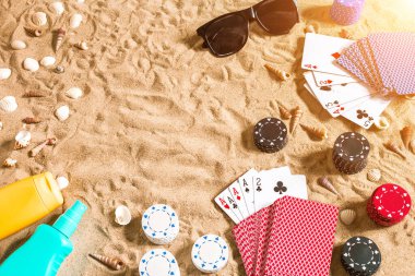 Plaj pokeri. Çipler ve kartlar kumsalda. Deniz kabukları, güneş gözlüğü ve güneş kremi. Üst Manzara. Uzayı kopyala Düz yatıyordu. Güneş parlaması
