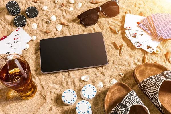 Online poker game on the beach with digital tablet and stacks of chips. Top view. Copy space. Flat lay. Sun flare