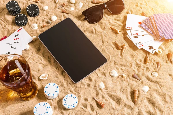 Online poker game on the beach with digital tablet and stacks of chips. Top view. Copy space. Flat lay. Sun flare