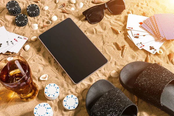 Online poker game on the beach with digital tablet and stacks of chips. Top view. Copy space. Flat lay. Sun flare