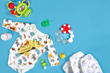 Babies goods: cloth diaper, baby powder, nibbler, cream, teether, soother, baby toy on blue background. Copy space. Top view. Early childhood development concept clipart