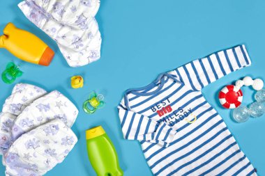Baby care with bath set. Nipple, toy, clothes, shampoo on blue background top view mockup. Flat lay. Still life. Copy space