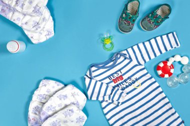Babies goods: cloth diaper, baby powder, nibbler, cream, teether, soother, baby toy on blue background. Copy space. Top view. Early childhood development concept