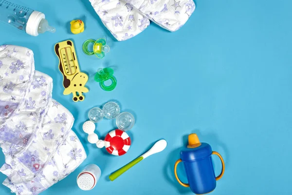 Babies goods: cloth diaper, baby powder, nibbler, cream, teether, soother, baby toy on blue background. Copy space. Top view. Early childhood development concept