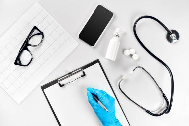Doktor masası, aletler, tıbbi aletler, steteskop, hastanede beyaz arka plan yatağı üzerinde çalışmak. Doktorlar mavi bir eldiven verdiler. Göstergeleri boş bir kağıtta gösterdiler. Üst Manzara. Devam et