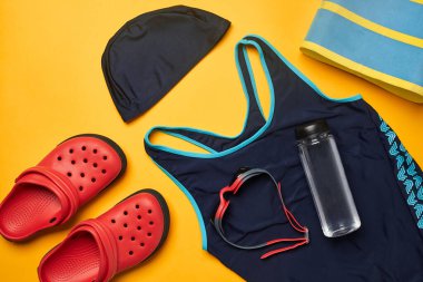 Havuz aksesuarları, mavi mayo, yüzme şapkası ve gözlük, çizgili havlu, kırmızı terlik ve sarı arka planda su için şeffaf şişe gibi. Çok renkli plaj kıyafeti. Boşluğu kopyala