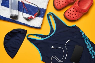 Mavi mayo, yüzme şapkası ve gözlükler, çizgili havlu, kırmızı terlik, beyaz kulaklıklı siyah akıllı telefon ve sarı arka plan üzerine şişe gibi düz yatıyordu yaz havuzu aksesuarları. Renkli plaj