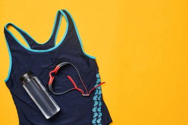 Havuz aksesuarları, mavi mayo, kırmızı yüzme gözlüğü ve sarı arka planda bir şişe. Çok renkli plaj kıyafeti. Boşluğu kopyala, üst görünüm, yakın plan.