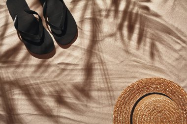 Tropikal palmiye yapraklarının gölgesi olan yaz konsepti. Siyah tanga ve hasır şapka gibi gezgin tatil aksesuarları beyaz bir kumsalda serilmiştir. Yaz mevsimi yaşam tarzı