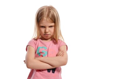 Close-up portrait of a charming blonde little lady with a long hair, in a pink t-shirt, looking offended while posing isolated on white background with copy space. Concept of a joyful childhood.