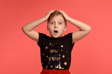 Close-up shot of a pretty blonde little lady in a combined dress, looking shocked while posing against a pink background with copy space. Concept of a happy childhood.