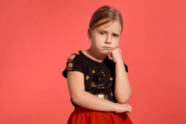 Close-up shot of a pretty blonde little female in a combined dress, looking disappointed while posing against a pink background with copy space. Concept of a happy childhood.