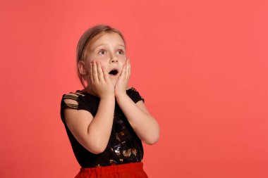 Close-up shot of a beautiful blonde little lady in a combined dress, looking at something with a wondered face while posing against a pink background with copy space. Concept of a happy childhood.