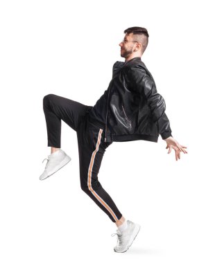 Full-length photo of a modern performer in glasses, black leather jacket, t-shirt, sports pants and light sneakers fooling around sideways in studio. Indoor photo of an athletic man dancing and
