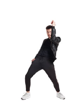 Full-length photo of a modern performer in glasses, black leather jacket, t-shirt, sports pants and light sneakers fooling around in studio. Indoor photo of an attractive person dancing isolated on