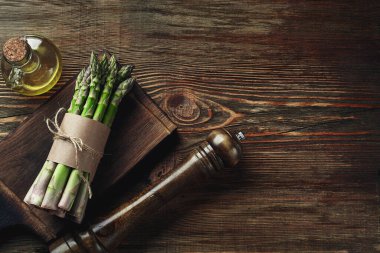 Bunch of an edible, juicy spears of asparagus on wooden background. Fresh, green vegetables with olive oil and seasonings, kitchen pestle, top view. Healthy eating. Fall harvest, agricultural farming