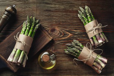 Bunches of an edible, juicy stems of asparagus on wooden background. Fresh, green vegetables with olive oil and seasonings, kitchen pestle, top view. Healthy eating. Fall harvest, agricultural farming