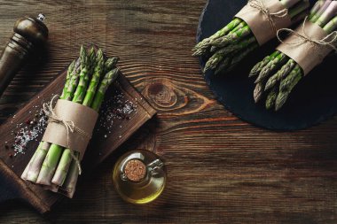 Bunches of an edible, uncooked spears of asparagus on wooden background. Fresh, green vegetables with olive oil and seasonings, top view. Healthy eating. Fall harvest, agricultural farming concept.