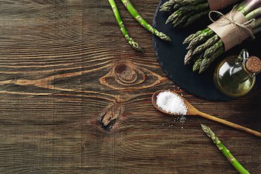 Bunch of an edible, green spears of asparagus on wooden background. Fresh vegetables with olive oil and seasonings, top view. Healthy eating. Fall harvest, agricultural farming concept.