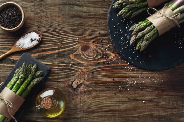 Bunches of an edible, fresh stalks of asparagus on wooden background. Green vegetables with olive oil and seasonings, top view. Healthy meal. Fall harvest, agricultural farming concept.