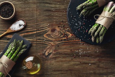 Bunches of an edible, fresh stems of asparagus on wooden background. Green vegetables with olive oil and seasonings, top view. Healthy meal. Fall harvest, agricultural farming concept.