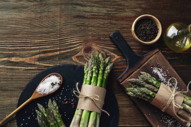 Bunches of an edible, ripe stalks of asparagus on wooden background. Fresh, green vegetables with olive oil and seasonings, top view. Healthy meal. Fall harvest, agricultural farming concept.