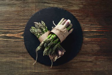 Bunches of an edible sprouts of asparagus on a stone slate, wooden background. Fresh, green vegetables, top view. Healthy food. Fall harvest, agricultural farming concept.