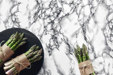 Bunch of an edible, uncooked sprigs of asparagus on a stone slate, marble background. Fresh, green vegetables, top view. Healthy eating. Spring harvest, agricultural farming concept.