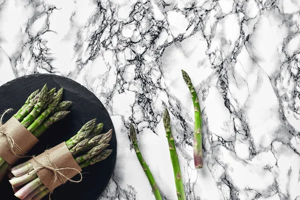 Bunch of an edible, juicy stems of asparagus on a stone slate, marble background. Fresh, green vegetables, top view. Healthy eating. Spring harvest, agricultural farming concept.