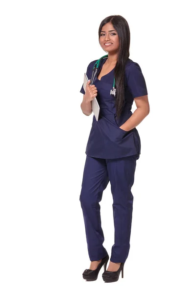 年轻的印度医生妇女的肖像与听诊器在脖子附近查出在白色背景 她穿着蓝色制服拿着记事本 在镜头前摆姿势 — 图库照片