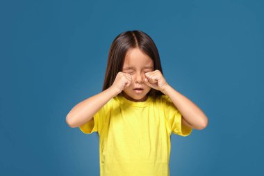 Sad offended little girl in yellow t-shirt cries on blue background