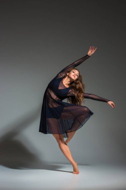 Young beautiful dancer in black dress posing on a dark gray studio background. Modern, Contemporary, improvisation