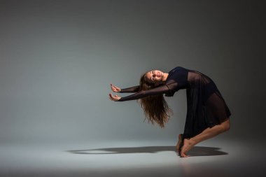Young beautiful dancer in black dress posing on a dark gray studio background. Modern, Contemporary, improvisation