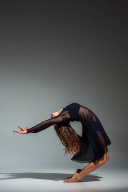 Young beautiful dancer in black dress posing on a dark gray studio background. Modern, Contemporary, improvisation