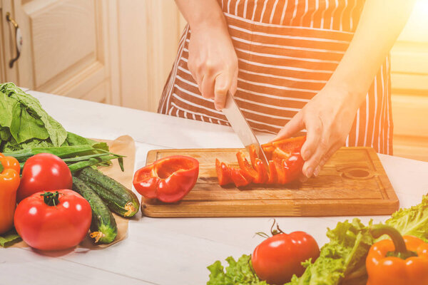 Young woman cooking in the kitchen at home. Healthy food. Diet. Dieting concept. Healthy lifestyle. Cooking at home. Prepare food. A woman cuts a pepper and vegetables with a knife.