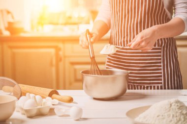 Kase hamur ve çırpma teli, closeup ile tutan genç kadın. Çizgili bir önlük bir kadın mutfakta yemek