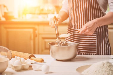 Kase hamur ve çırpma teli, closeup ile tutan genç kadın. Çizgili bir önlük bir kadın mutfakta yemek
